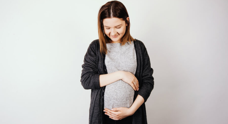 A pregnant woman smiling and gently holding her belly, symbolizing a healthy pregnancy supported by natural fertility care and holistic family planning.